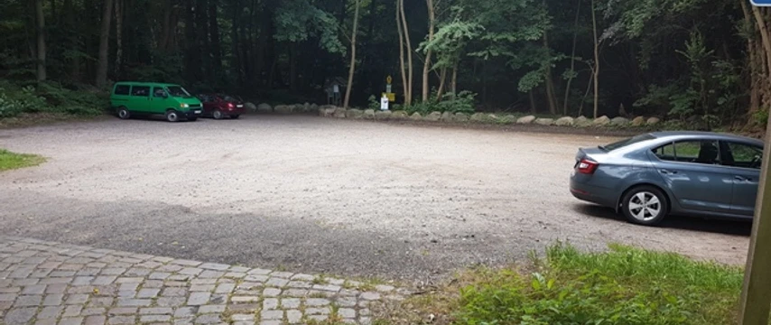 Wanderparkplatz Garrensee Sandparkplatz mit parkenden Autos. Im Hintergrund stehen Bäume