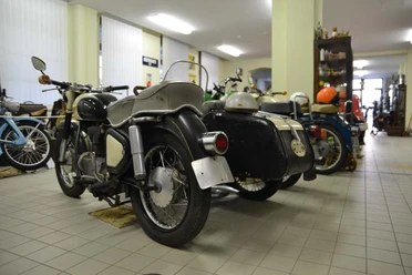 Oldtimer Schauwerkstatt Sebnitz Mehrere klassische Motorräder mit Beiwagen stehen in einem hellen Raum auf gefliesten Boden, umgeben von Regalen und Dekor.