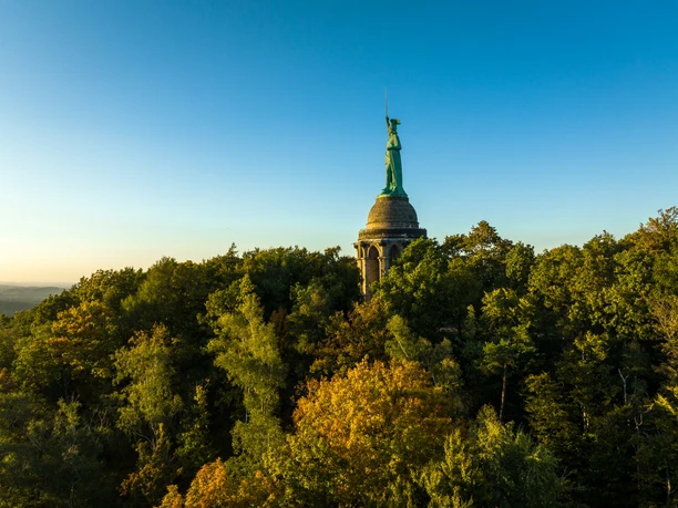 Detmold-Hermannsdenkmal-Teutoburger-Wald-Tourismus-D-Ketz-106.jpg Denkmal auf bewaldetem Hügel bei Sonnenuntergang, im Hintergrund blauer Himmel.