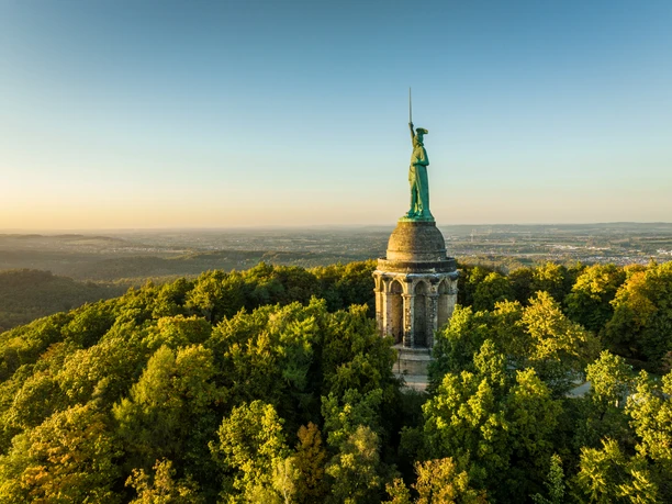 Detmold-Hermannsdenkmal-Teutoburger-Wald-Tourismus-D-Ketz-110.jpg Hermann-Denkmal im Teutoburger Wald bei Sonnenuntergang, umgeben von dicht bewaldeten Hügeln.
