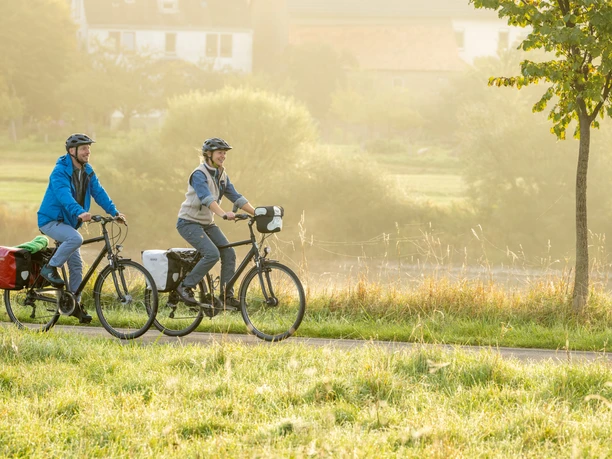 Hoexter-Godelheimer See-Weserradweg-Teutoburger-Wald-Tourismus-D-Ketz-012.jpg Zwei Personen radeln auf einem Pfad durch eine ländliche, sonnenbeschienene Landschaft.