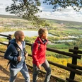 Hoexter-Rabenklippen-Teutoburger-Wald-Tourismus-D-Ketz-105.jpg Zwei Wanderer mit Rucksack genießen einen Panoramablick auf eine Flusslandschaft bei sonnigem Wetter.