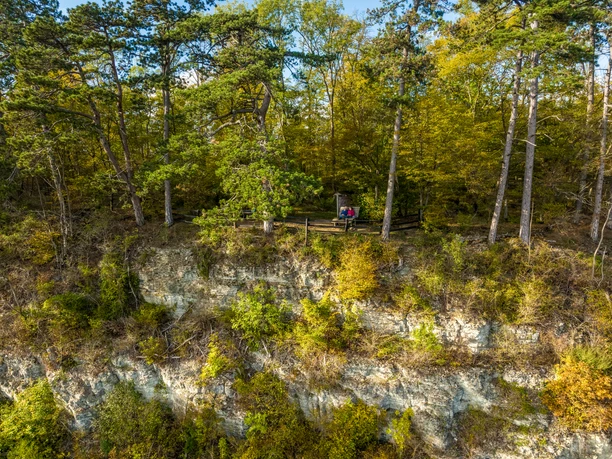 Eine bewaldete Klippe, auf der ein Paar auf einer Bank sitzt, umgeben von herbstlichen Bäumen.