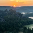 Sonnenaufgang im Basteigebiet Sonnenaufgang über einer nebligen Waldlandschaft mit markanten Felsformationen im Vordergrund.