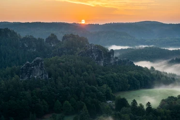 Zonsopgang in de omgeving van Bastei Zonsopgang boven een mistig boslandschap met opvallende rotsformaties op de voorgrond.
