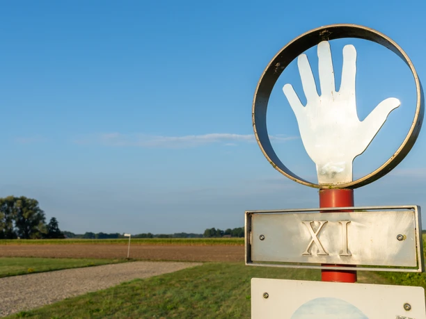 Ein Schild mit römischer Zahl XI und einer Hand vor einem Feld unter blauem Himmel.