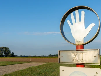 Delbrueck-Roemerlager-Teutoburger-Wald-Tourismus-Patrick-Gawandtka-018.jpg Ein Schild mit römischer Zahl XI und einer Hand vor einem Feld unter blauem Himmel.