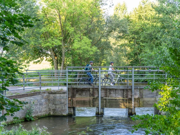 Delbrueck-BokerKanal-Teutoburger-Wald-Tourismus-Patrick-Gawandtka-034.jpg Zwei Radfahrer überqueren im Sommer mit ihren Fahrrädern eine schmale Holzbrücke über einen Bach.
