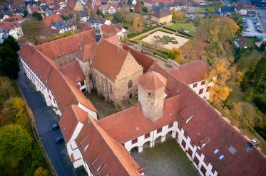 Luftaufnahme eines historischen Klosterkomplexes mit roten Ziegeldächern und Herbstbäumen.