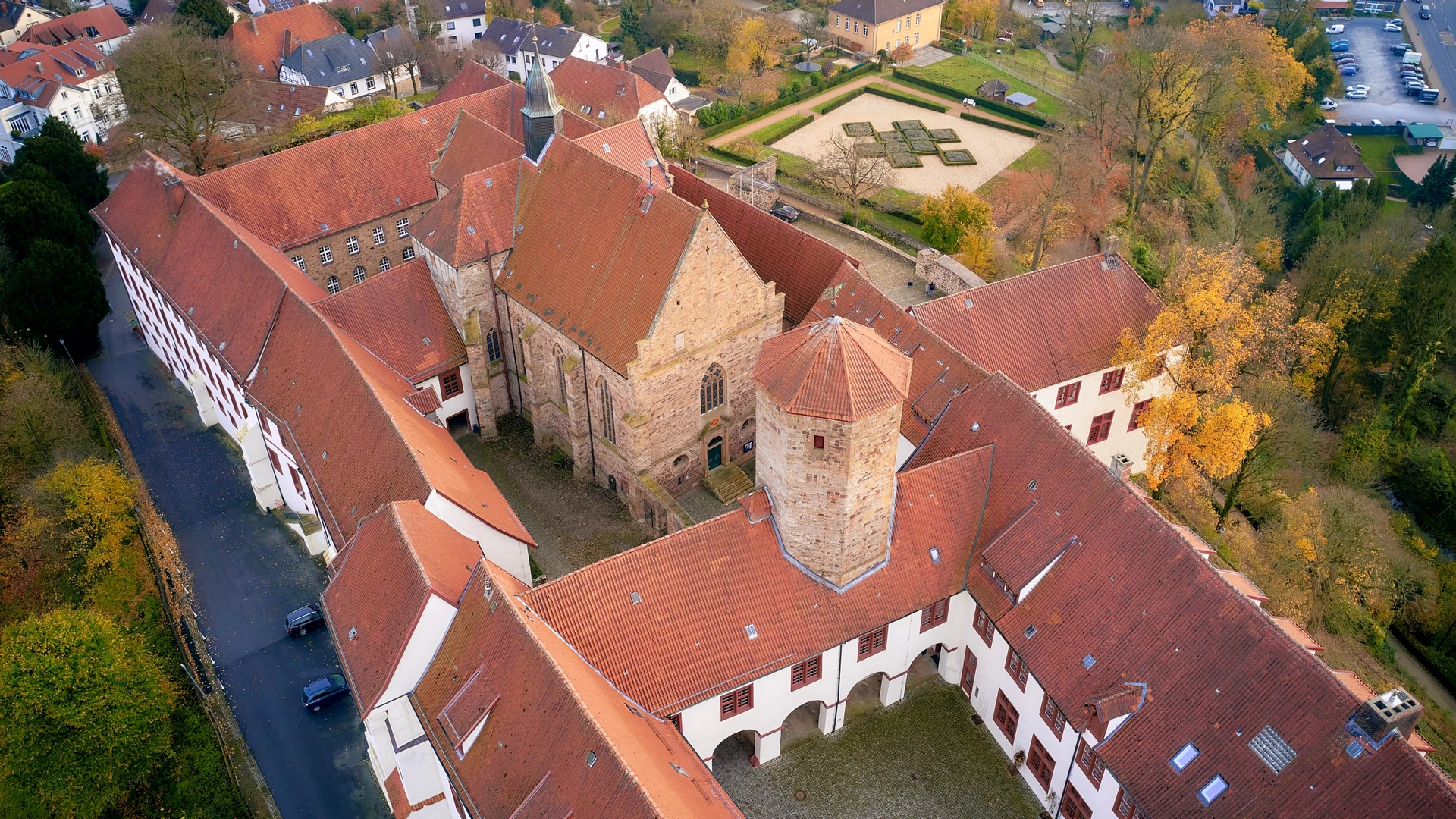 Aerial view of a historic monastery complex with red-tiled roofs and autumn trees.