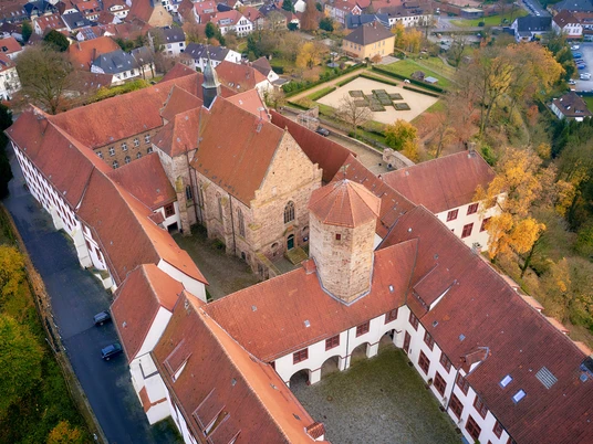 Luftaufnahme eines historischen Klosterkomplexes mit roten Ziegeldächern und Herbstbäumen.