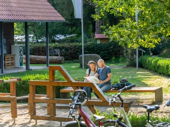 Hoevelhof-Ems-Infozentrum-Teutoburger-Wald-Tourismus-Patrick-Gawandtka-126.jpg Ein Paar sitzt auf einer Bank im sonnigen Park, umgeben von Fahrrädern und studiert eine Karte.