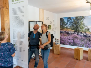 Ein Paar liest Informationen in einem Besucherzentrum, umgeben von Naturfotografien und Holzdekor.