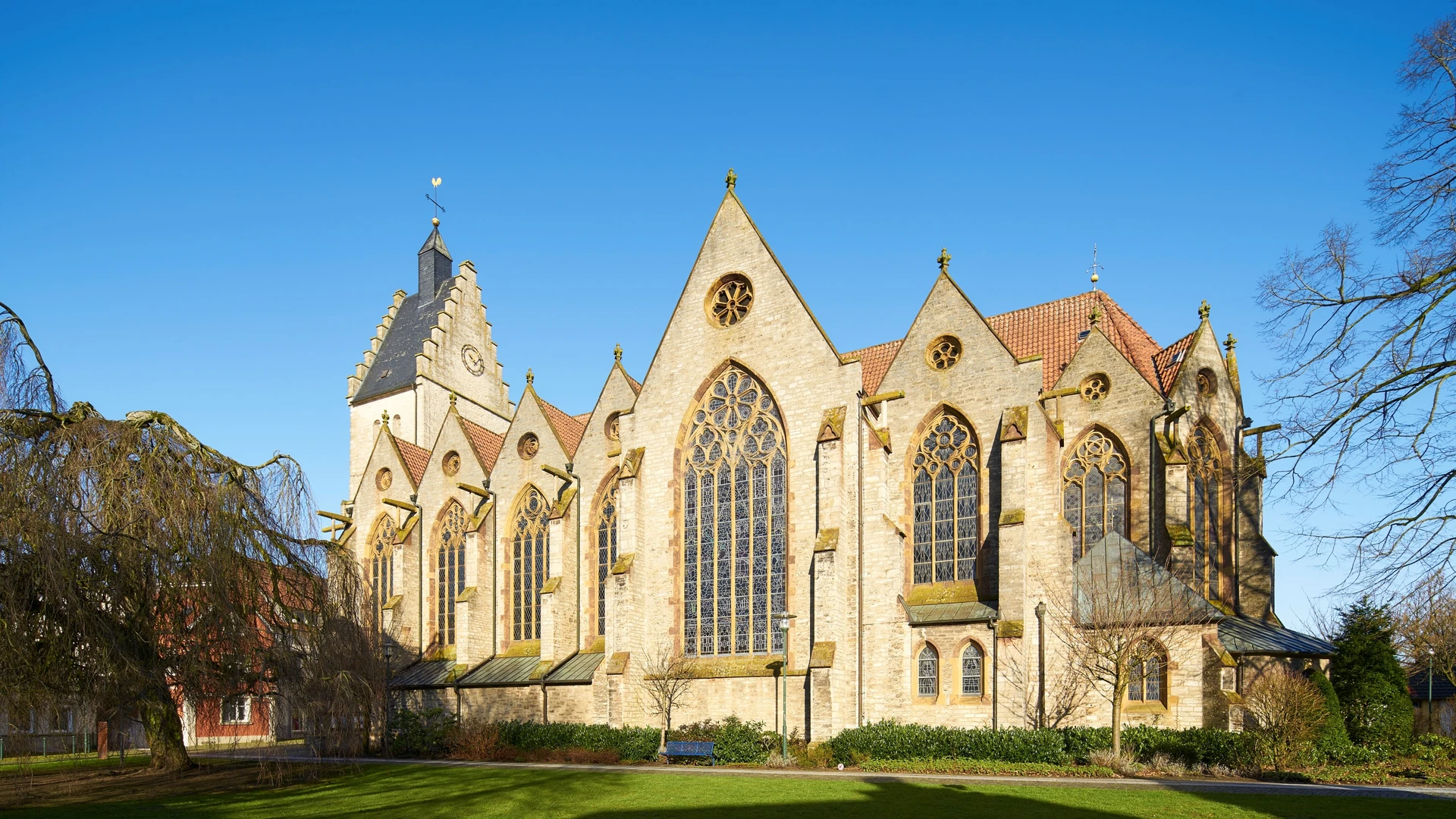 A Gothic church made of sandstone with large stained-glass windows and a well-manicured lawn in the foreground.