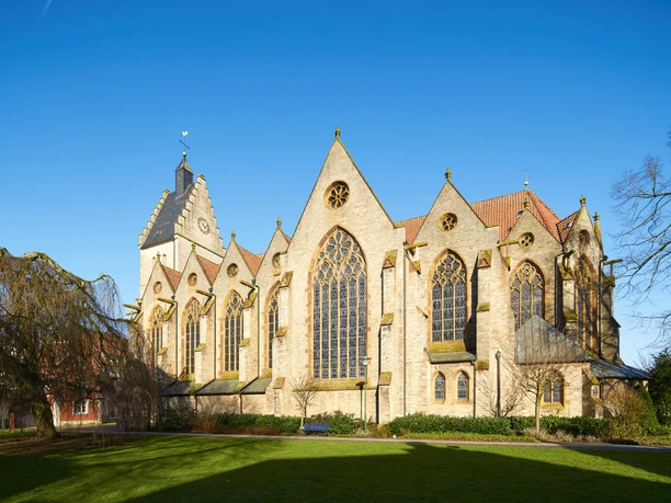 Gotische Kirche aus Sandstein mit großen Buntglasfenstern und gepflegtem Rasen im Vordergrund.