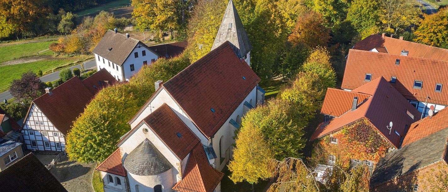 Aerial view of St. Urban Church in Bissendorf, surrounded by trees and buildings in autumn colors.