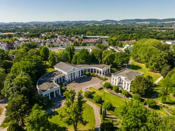 Bad Oeynhausen-Kurpark-Teutoburger-Wald-Tourismus-D-Ketz-084-CC-BY-SA.jpg Kurhaus Bad Oeynhausen: Historischer Bau mit Rundbogenfassade, umgeben von grüner Parklandschaft.