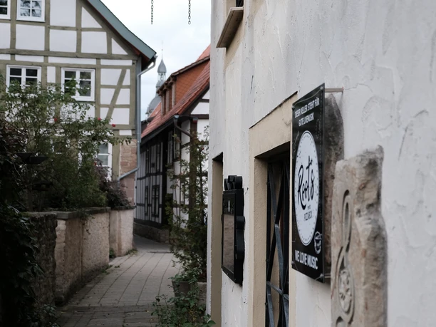 Eine enge Gasse mit Fachwerkhäusern und einem nostalgischen Laternenhalter an einer weiß verputzten Wand.