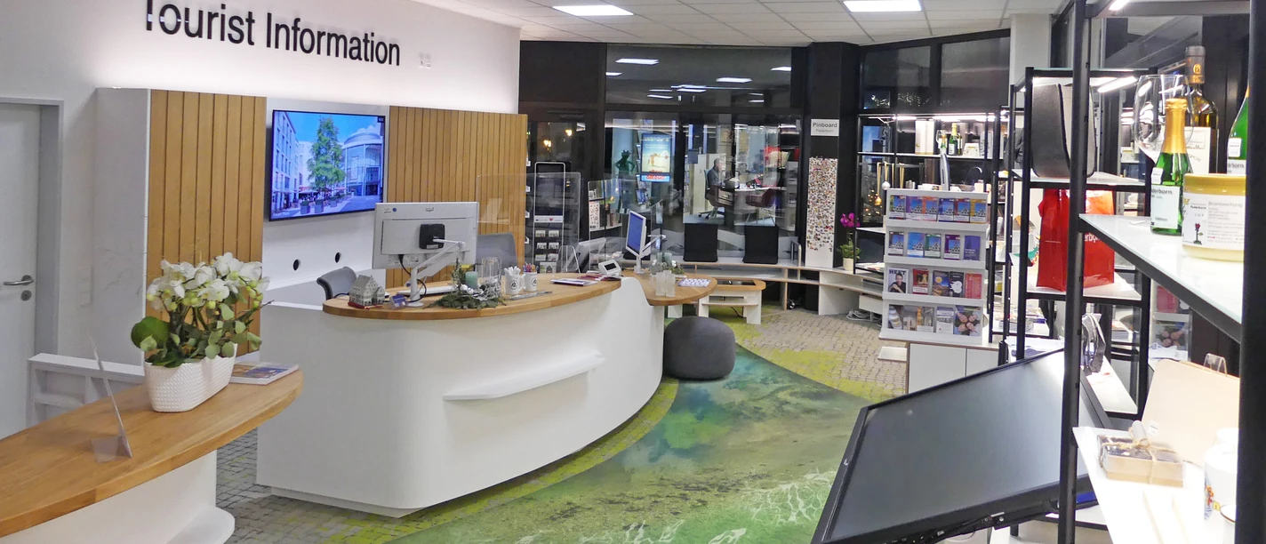 Tourist Information Paderborn Heller, moderner Raum der Tourist Information mit Info-Theke und Regalen voller Broschüren und Karten.