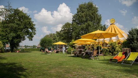 Schirmbar (Jens Butz).jpg Mehrere Personen sitzen unter Sonnenschirmen auf einer Wiese und genießen das schöne Wetter