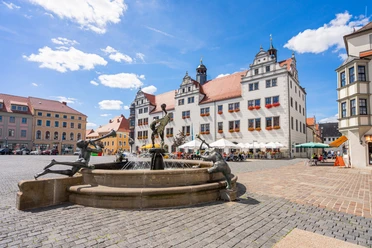 Marché de Torgau Fontaine sur la place du marché de Torgau, devant des bâtiments historiques, sous un ciel bleu.