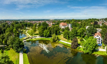 Kurpark Bad Salzuflen Der Bild zeigt einen weitläufigen Park mit grünen Wiesen, einem Teich und einem zentralen Wasserbrunnen.