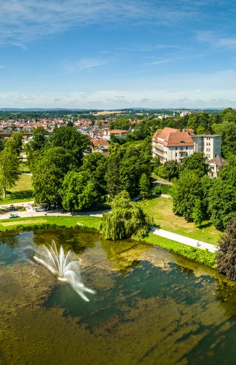 Kurpark Bad Salzuflen Der Bild zeigt einen weitläufigen Park mit grünen Wiesen, einem Teich und einem zentralen Wasserbrunnen.