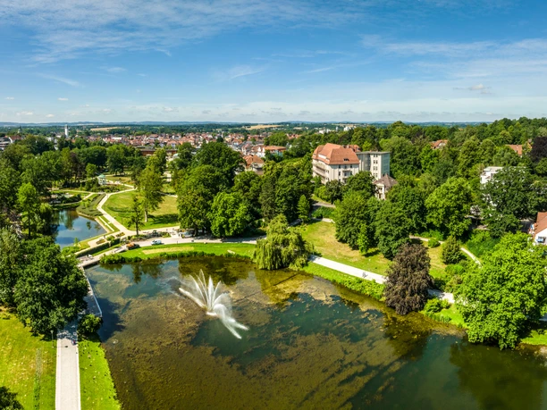 Kurpark Bad Salzuflen Der Bild zeigt einen weitläufigen Park mit grünen Wiesen, einem Teich und einem zentralen Wasserbrunnen.