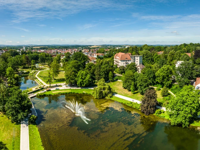 Kurpark Bad Salzuflen Der Bild zeigt einen weitläufigen Park mit grünen Wiesen, einem Teich und einem zentralen Wasserbrunnen.