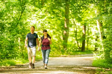 Bad Salzuflen-VitalWanderWelt-Teutoburger-Wald-Tourismus-D-Ketz-066.jpg Zwei Personen spazieren auf einem sonnendurchfluteten Waldweg, umgeben von üppigem grünen Laub.