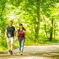 Bad Salzuflen-VitalWanderWelt-Teutoburger-Wald-Tourismus-D-Ketz-066.jpg Zwei Personen spazieren auf einem sonnendurchfluteten Waldweg, umgeben von üppigem grünen Laub.