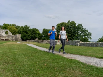 Bueren_BurgruineRingelstein_Teutoburger-Wald-Tourismus-Patrick-Gawandtka-096.jpg Ein Paar spaziert fröhlich auf einem Pfad durch eine grüne Wiese, mit Burgruine im Hintergrund.