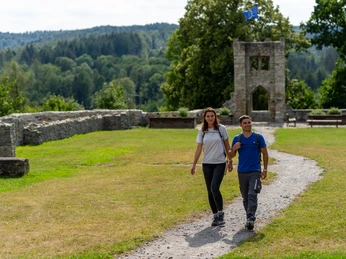 Bueren_BurgruineRingelstein_Teutoburger-Wald-Tourismus-Patrick-Gawandtka-104.jpg Zwei Personen wandern auf einem Pfad vor einer alten Ruine in einer Waldlandschaft.