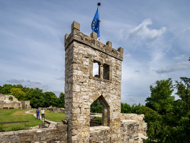 Mittelalterlicher Steinturm der Burg Landeck, mit einer EU-Flagge, umgeben von grüner Natur.