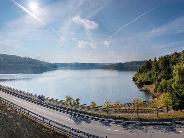 BadWuennenberg–Aabachtalsperre-Teutoburger-Wald-Tourismus-Patrick-Gawandtka-038-CC-BY-SA.jpg Stausee mit Radweg im Vordergrund, umgeben von dichtem, grünen Wald unter klarem blauen Himmel.