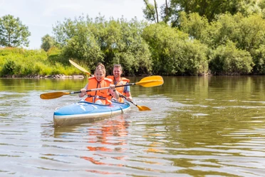 Beverungen-Bootshaus-Teutoburger-Wald-Tourismus-A-Röser-081.jpg Zwei Personen im Kanu mit Schwimmwesten paddeln auf einem ruhigen Fluss, umgeben von Bäumen.