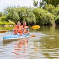 Beverungen-Bootshaus-Teutoburger-Wald-Tourismus-A-Röser-081.jpg Zwei Personen im Kanu mit Schwimmwesten paddeln auf einem ruhigen Fluss, umgeben von Bäumen.Twee mensen in een kano met zwemvest peddelen over een kalme rivier omringd door bomen.Two people in a canoe with life jackets paddling on a calm river surrounded by trees.