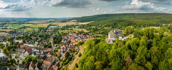 Schieder-Schwalenberg-Teutoburger-Wald-Tourismus-D-Ketz-040.jpg Luftaufnahme von Burg Hohenstein auf einem bewaldeten Hügel, umgeben von einem malerischen Dorf.
