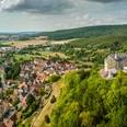 Schieder-Schwalenberg-Teutoburger-Wald-Tourismus-D-Ketz-040.jpg Luftaufnahme von Burg Hohenstein auf einem bewaldeten Hügel, umgeben von einem malerischen Dorf.