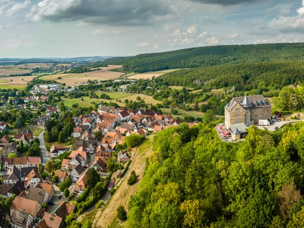 Schieder-Schwalenberg-Teutoburger-Wald-Tourismus-D-Ketz-040.jpg Luftaufnahme von Burg Hohenstein auf einem bewaldeten Hügel, umgeben von einem malerischen Dorf.
