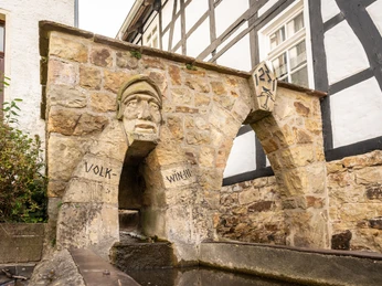 Steinbrunnen in Fachwerkfassade integriert, mit steinernem Gesicht und Inschrift "Volkwina".
