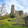 Burg Stolpen Die Burg Stolpen mit hohen, grauen Mauern auf einem grünen Hügel, umgeben von herbstlichen Bäumen unter blauem Himmel.