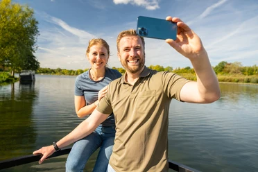 Schieder-Schwalenberg-Schiedersee-Teutoburger-Wald-Tourismus-D-Ketz-085.jpg Ein lächelndes Paar steht auf einem Steg und macht ein Selfie vor einem See mit blauem Himmel.
