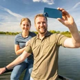 Schieder-Schwalenberg-Schiedersee-Teutoburger-Wald-Tourismus-D-Ketz-085.jpg Ein lächelndes Paar steht auf einem Steg und macht ein Selfie vor einem See mit blauem Himmel.