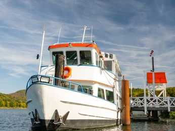 Schieder-Schwalenberg-Schiedersee-Teutoburger-Wald-Tourismus-D-Ketz-075.jpg Ein weißes Ausflugsschiff mit orangefarbenem Dach liegt an einem sonnigen Tag an einem Steg vor Anker.