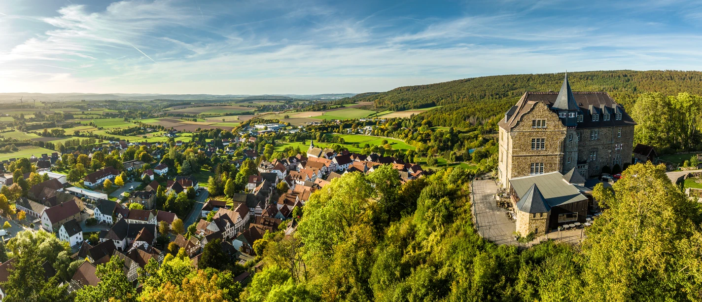 Schieder-Schwalenberg-Grafenblick-Teutoburger-Wald-Tourismus-D-Ketz-118-CC-BY-SA.jpg Luftaufnahme eines malerischen Dorfes in hügeliger Landschaft mit historischem Schloss am rechten Bildrand.