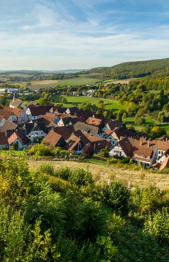 Ein Panoramablick auf ein idyllisches Dorf umgeben von grünen Hügeln und dicht bewaldeter Landschaft.