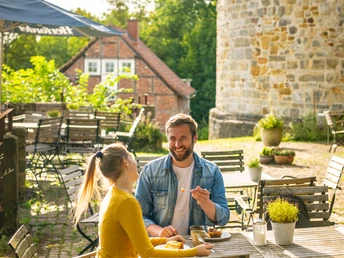 Ein Paar genießt eine Mahlzeit im Freien vor einem historischen, steinernen Burgmauerturm.