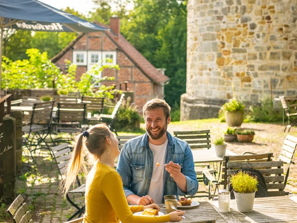 Borgholzhausen-Burg Ravensberg-Teutoburger-Wald-Tourismus-D-Ketz-088.jpg Ein Paar genießt eine Mahlzeit im Freien vor einem historischen, steinernen Burgmauerturm.