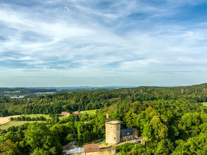 Luftaufnahme der mittelalterlichen Burg Ravensberg im Teutoburger Wald, umgeben von dichten Wäldern.